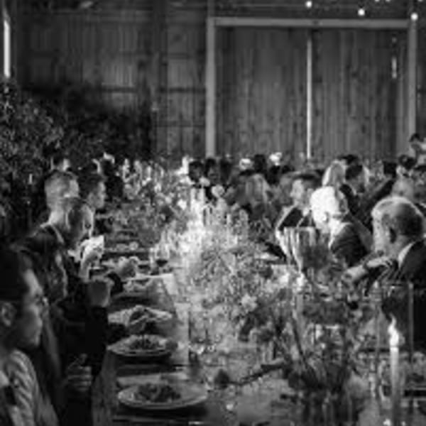 Black and white image of guests dining at long tables in a rustic barn setting.