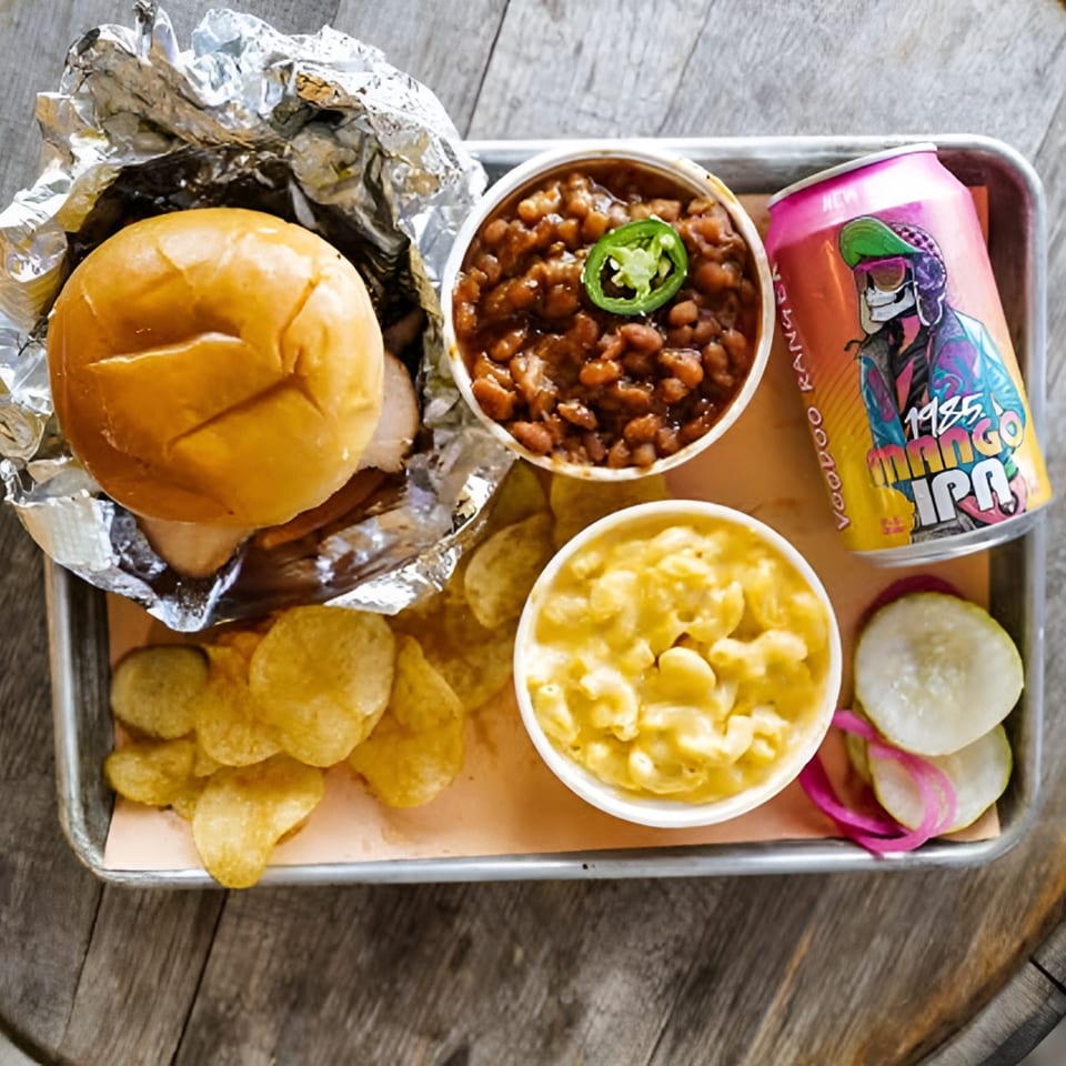 LX BBQ tray with a pulled pork sandwich, baked beans, mac and cheese, chips, pickles, and a beer.