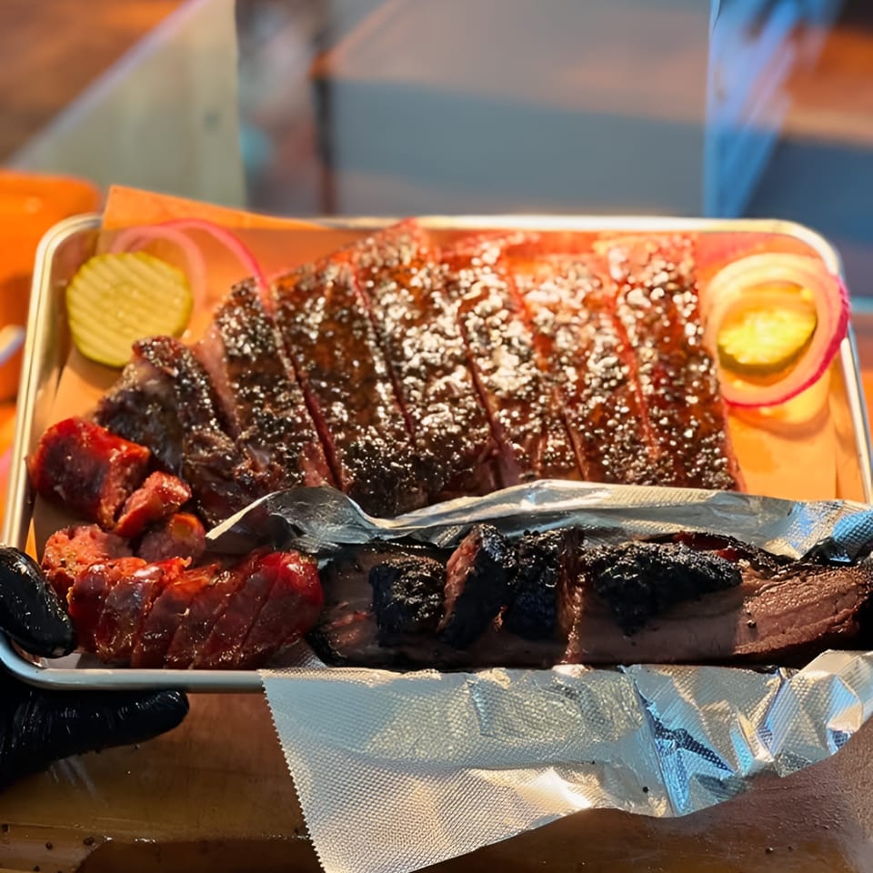 A tray of LX BBQ brisket, sausage, and burnt ends with pickles and red onion.