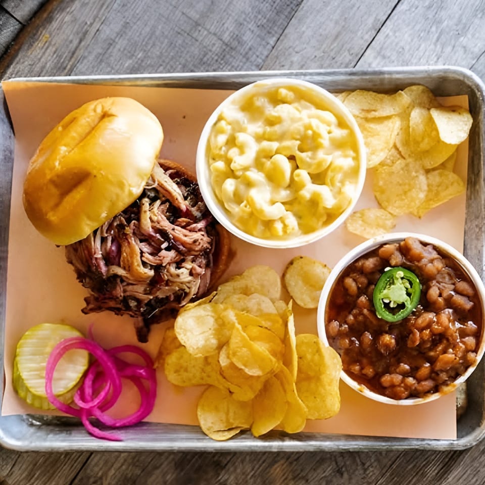 LX BBQ pulled pork sandwich with mac and cheese, baked beans, chips, pickles, and onions.