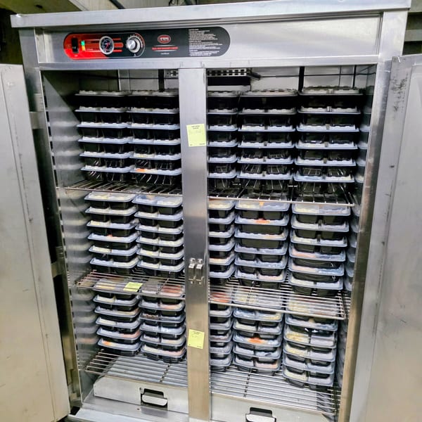 A large, stainless steel warming cabinet filled with numerous stacked meal prep containers from LX BBQ.
